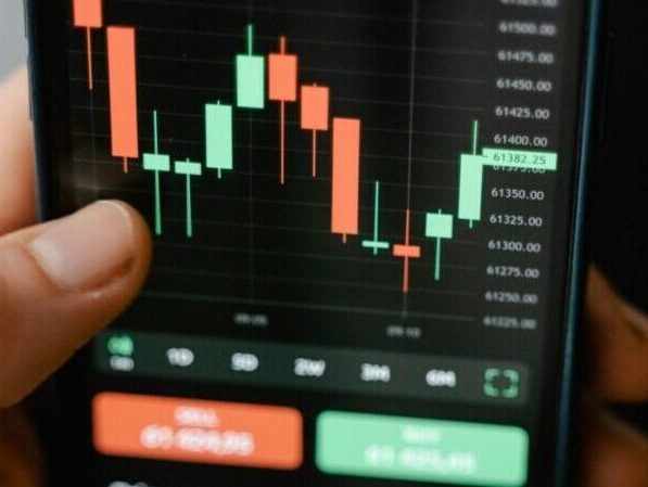 Hand holding smartphone displaying cryptocurrency trading graph in app.